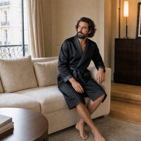 Modelo con bata negra para hombre con ribete gris azulado, sentado en un salón elegante